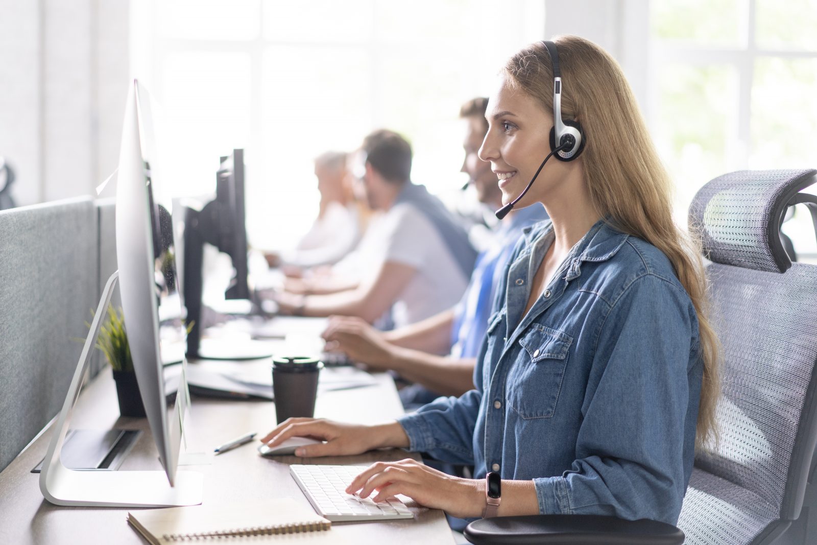 How can I help you? Beautiful call center workers in headphones are working at modern office